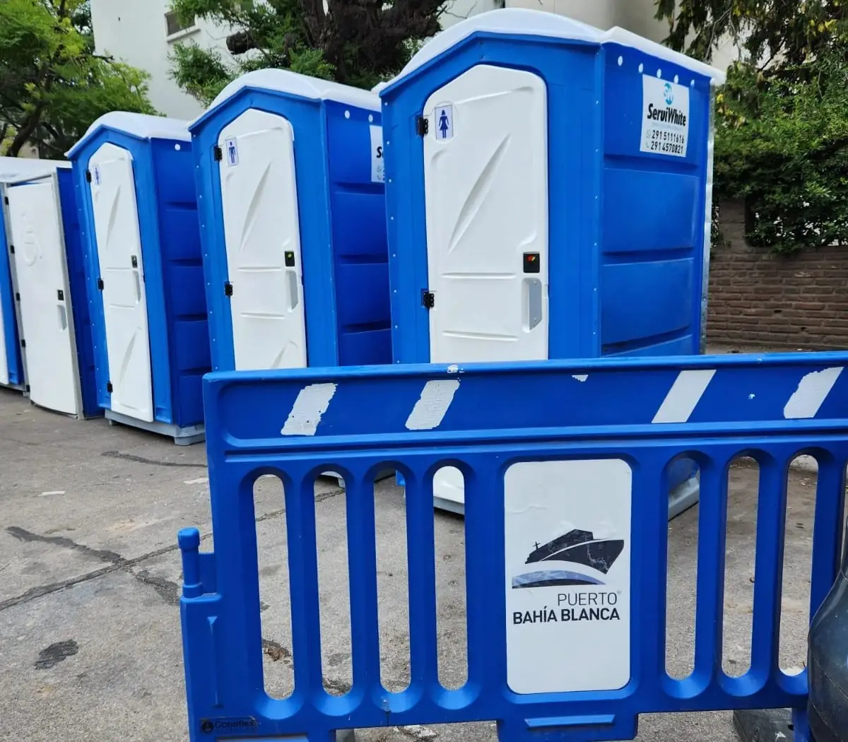 Baños químicos azules Serviwhite en un evento, detrás de una valla del Puerto Bahía Blanca