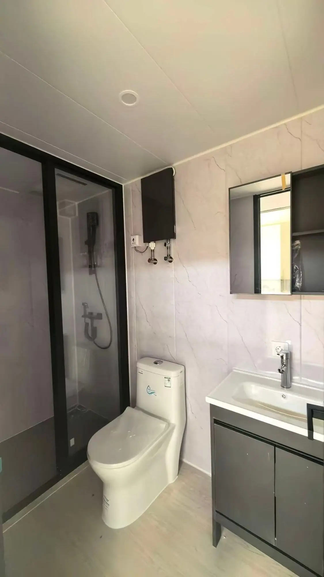 Baño de una Apple Cabin con ducha de mampara, inodoro, vanitory con espejo y calefón eléctrico