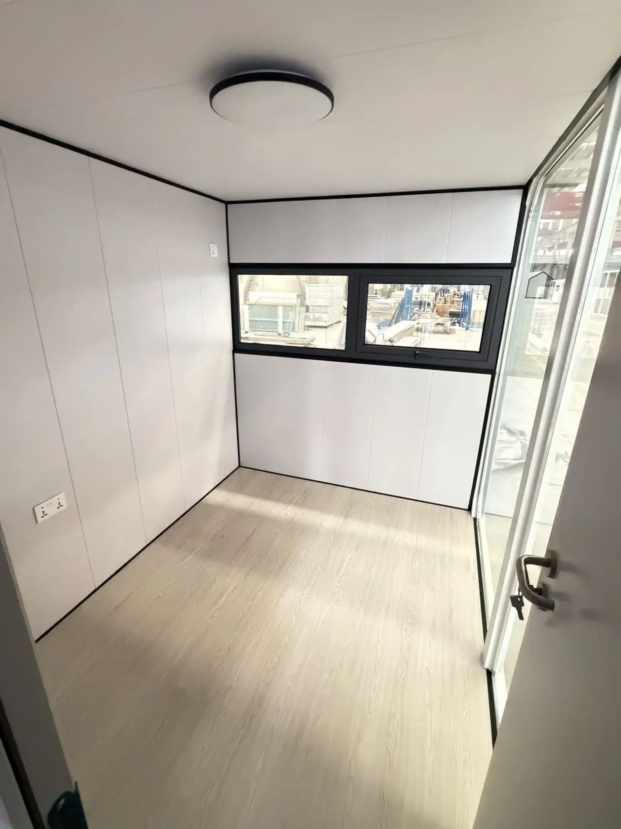 Dormitorio de una Apple Cabin con ventanas altas, plafón LED, tomas y el frente vidriado a un costado