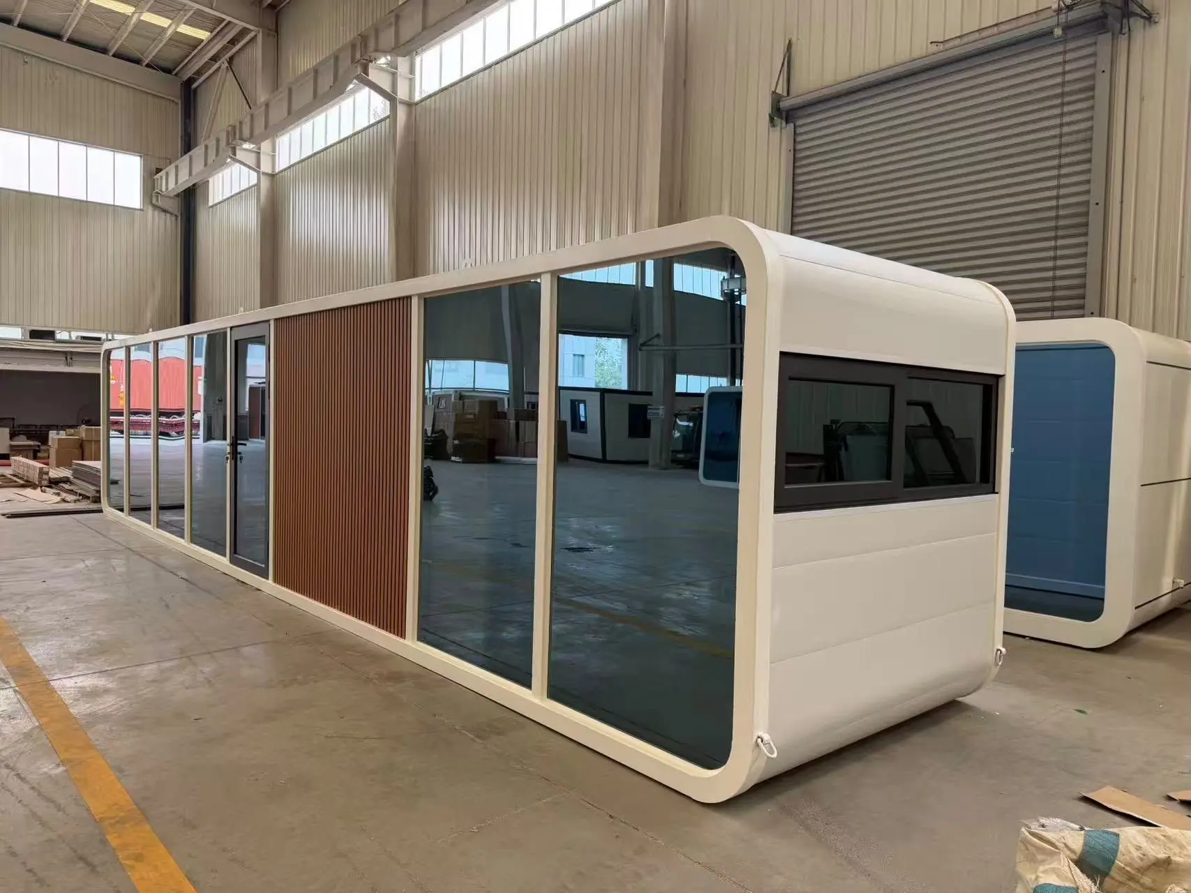 Apple Cabin blanca con frente vidriado de piso a techo y paño de listones símil madera
