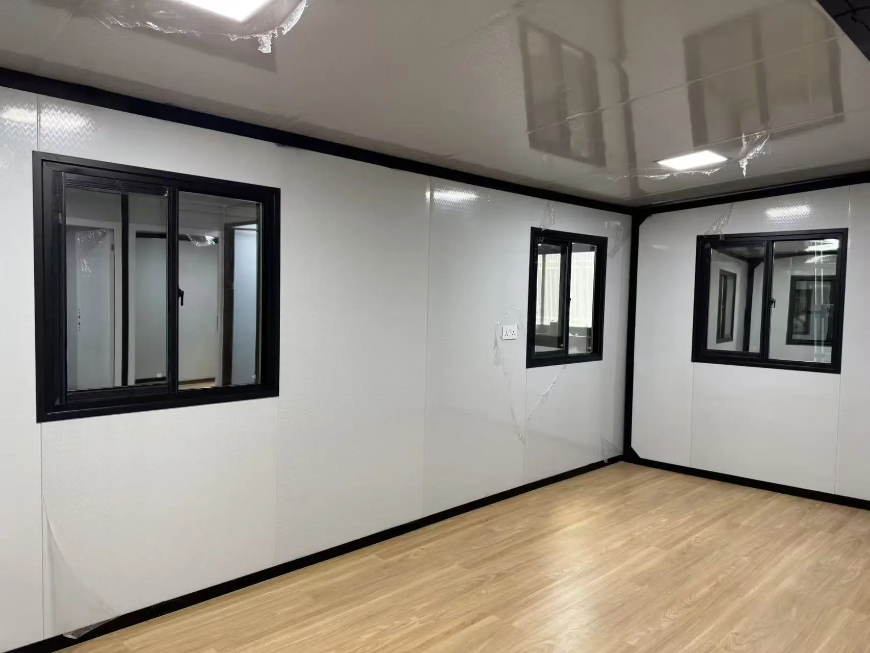 Ambiente amplio de una casa expandible con tres ventanas corredizas, paredes blancas y piso símil madera