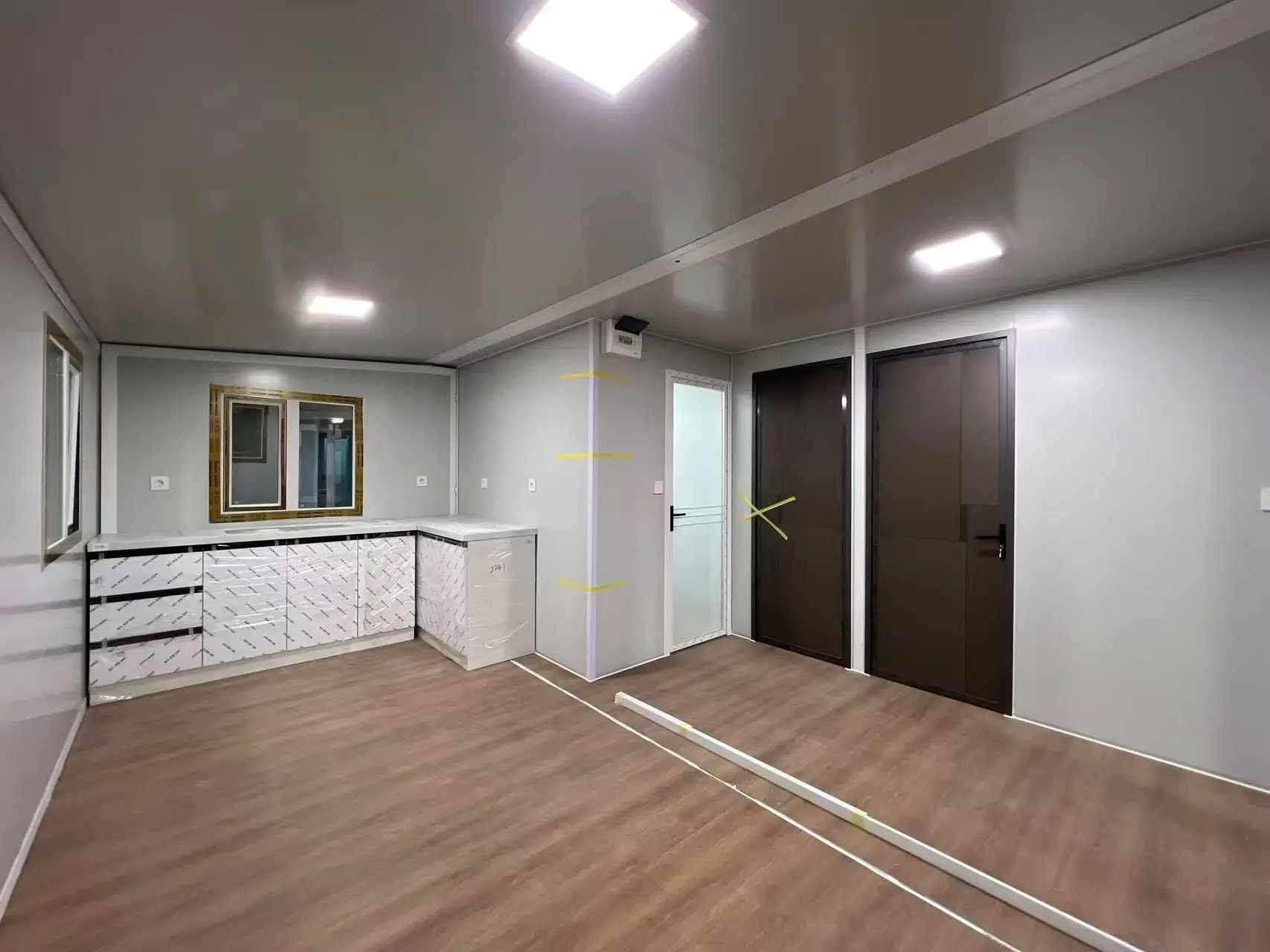 Living de una casa expandible con cocina en L, piso símil madera, luces LED y puertas a los dormitorios y al baño
