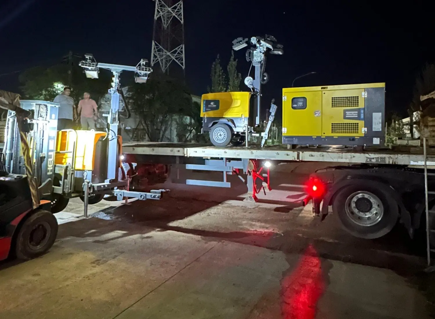 Autoelevador Heli carga una torre de iluminación sobre un semirremolque de noche, con un grupo electrógeno ya cargado
