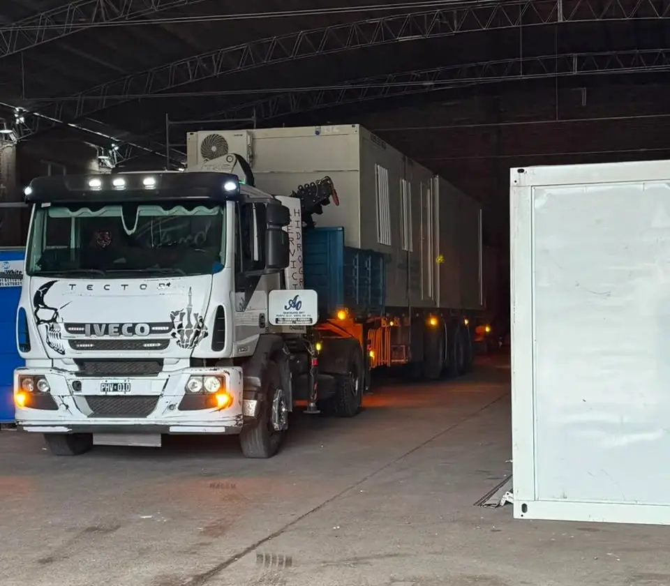 Camión Iveco con módulos habitacionales cargados saliendo del galpón