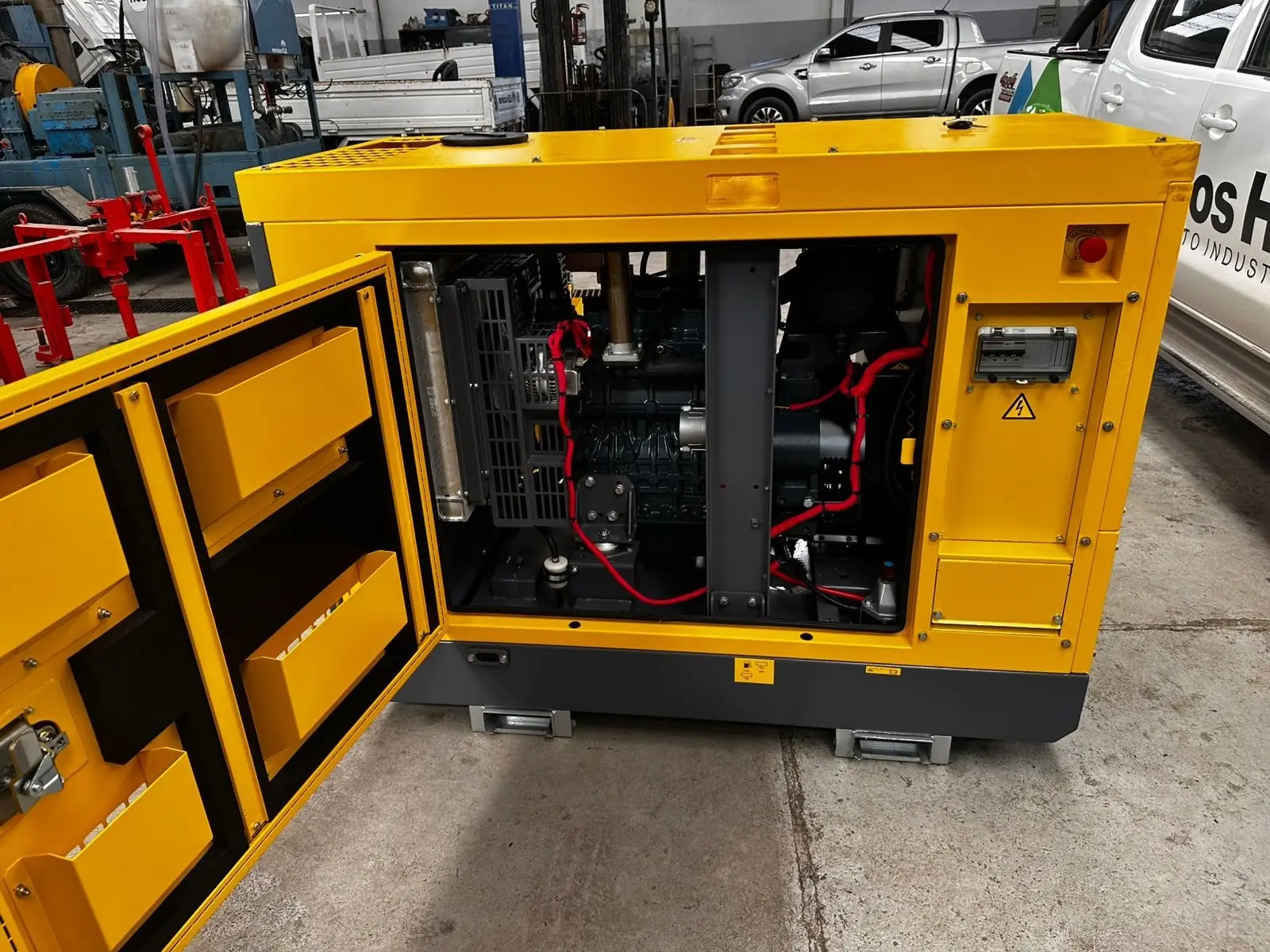 Grupo electrógeno Atlas Copco amarillo con la puerta abierta mostrando el motor, en el taller