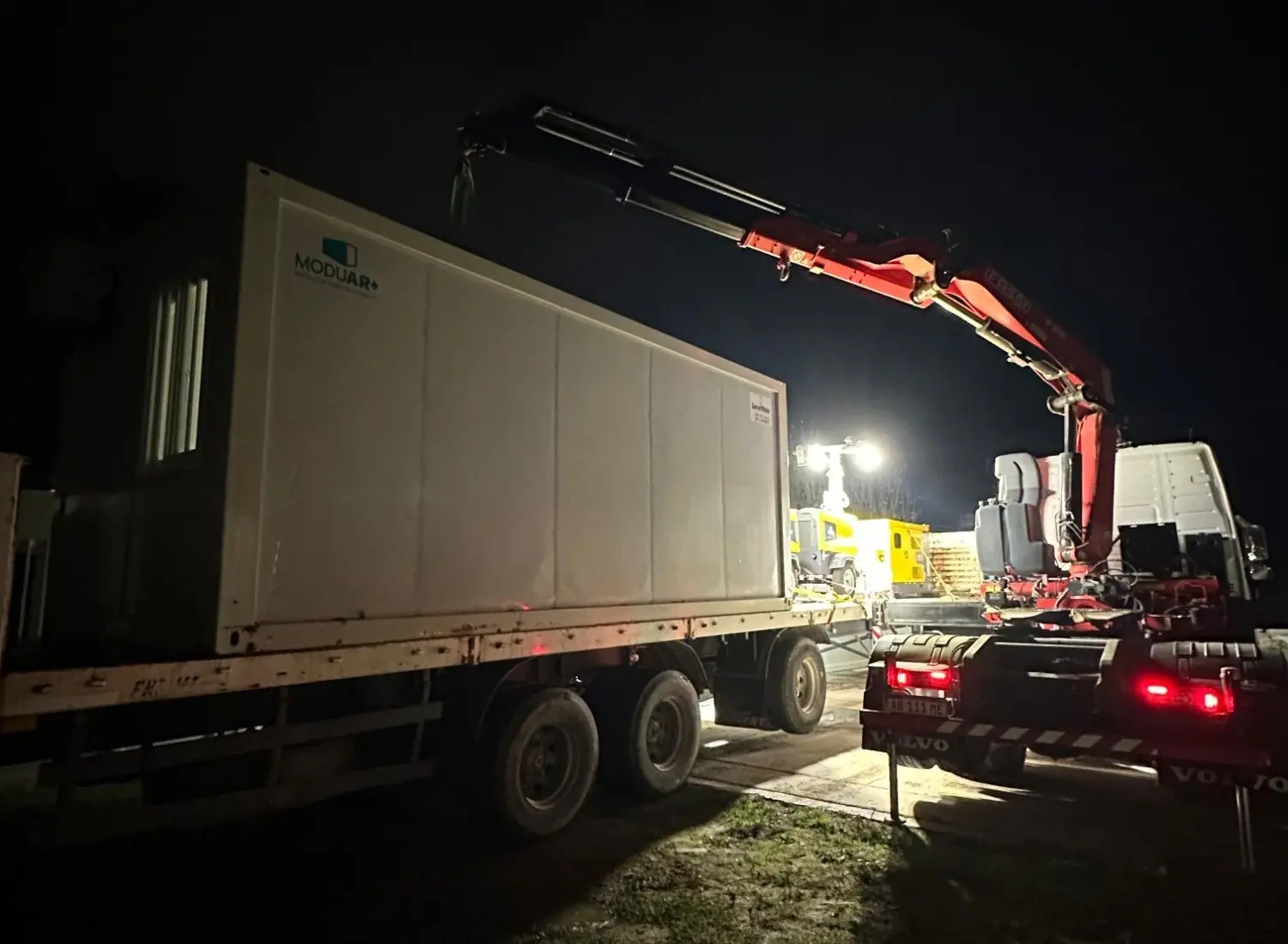 Hidrogrúa sobre camión levanta un módulo habitacional de noche