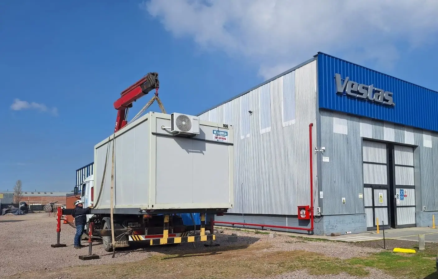 Hidrogrúa sobre camión descarga un módulo con aire acondicionado frente a la planta de Vestas