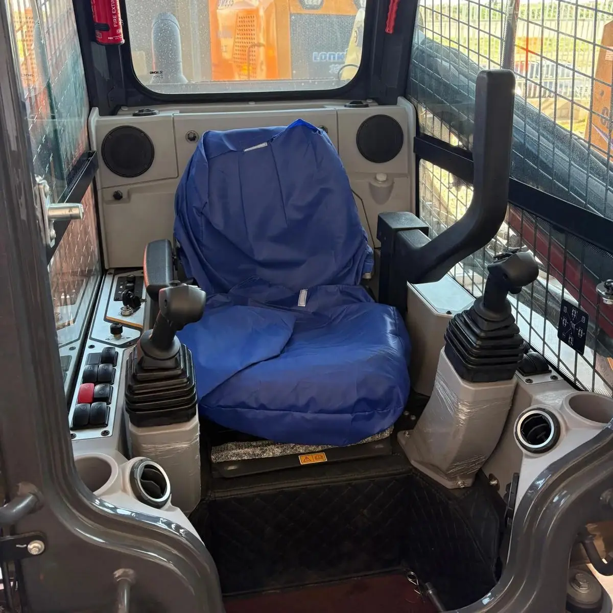 Cabina de una minicargadora XCMG con joysticks, matafuego y asiento con funda