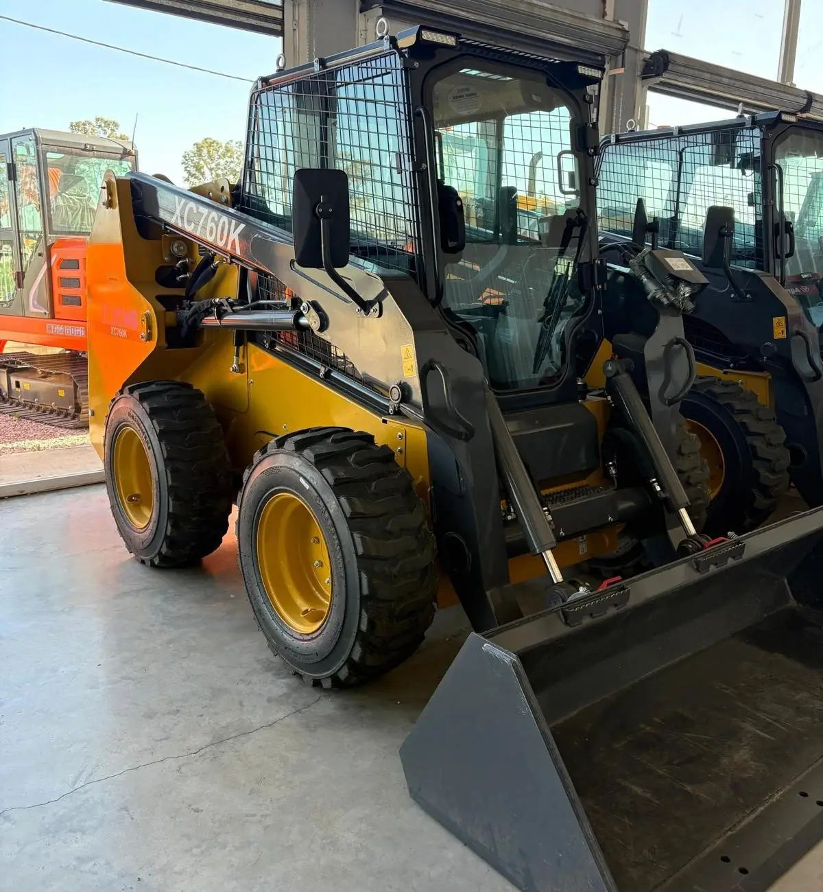 Minicargadora XCMG XC760K con cabina enrejada y balde, en el galpón junto a otras minicargadoras