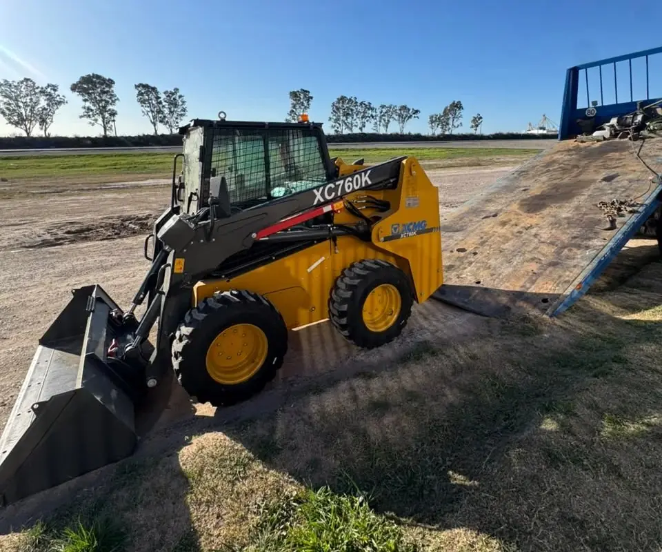 Minicargadora XCMG XC760K con balde junto a la rampa de un camión