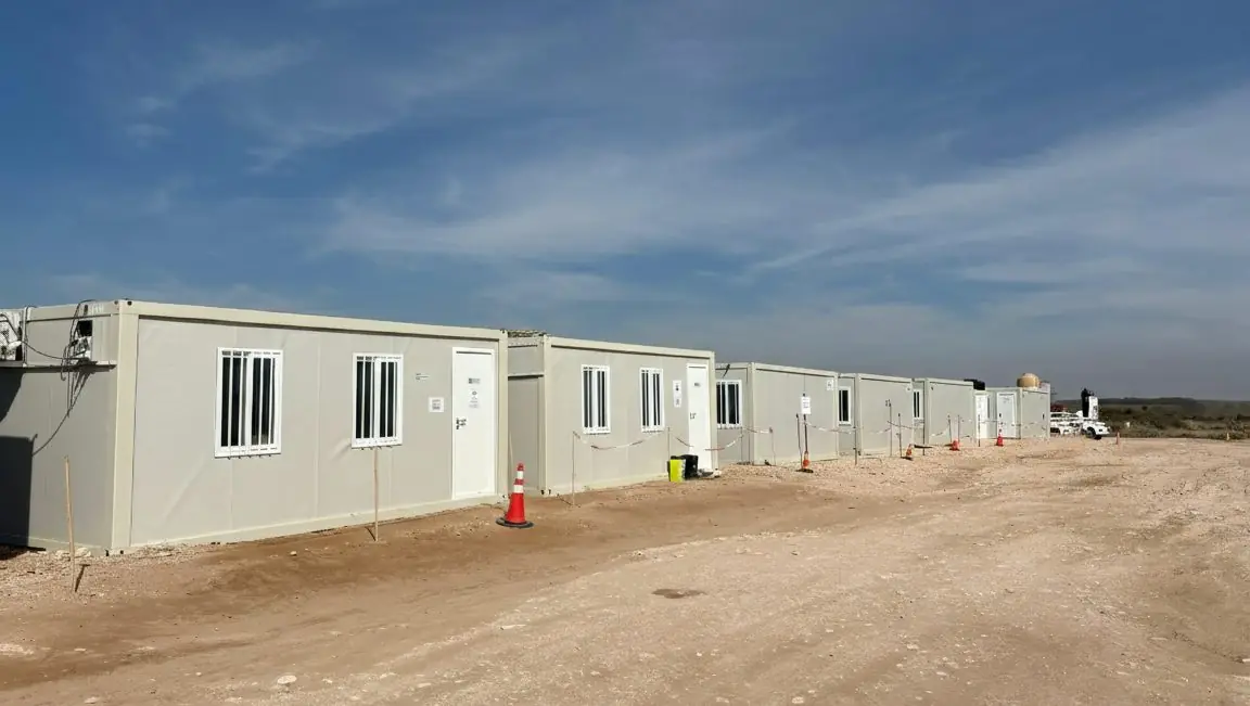 Hilera de módulos blancos con ventanas enrejadas instalados en un obrador sobre terreno de tierra