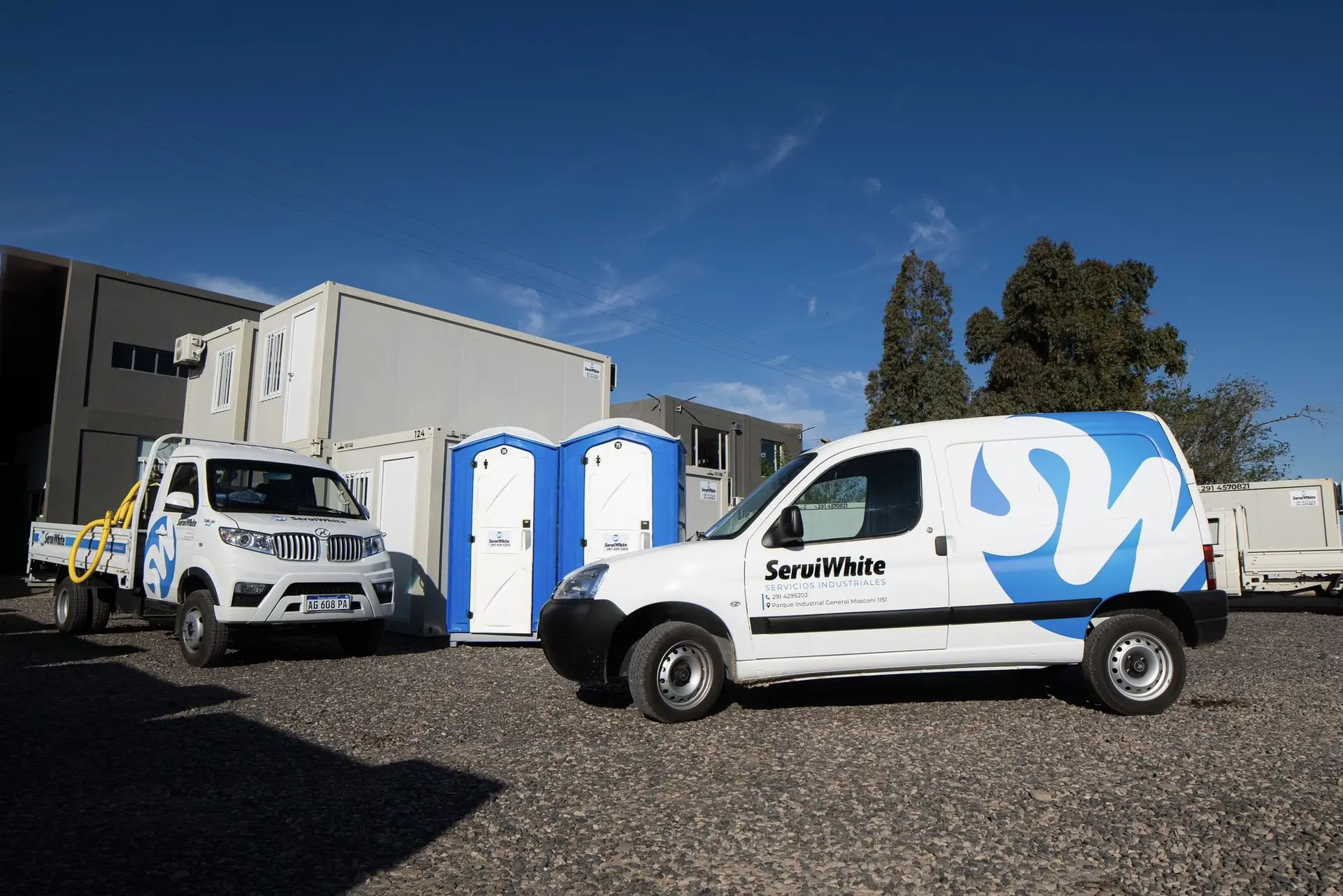 Camioneta y utilitario Serviwhite junto a baños químicos azules y módulos apilados en un playón
