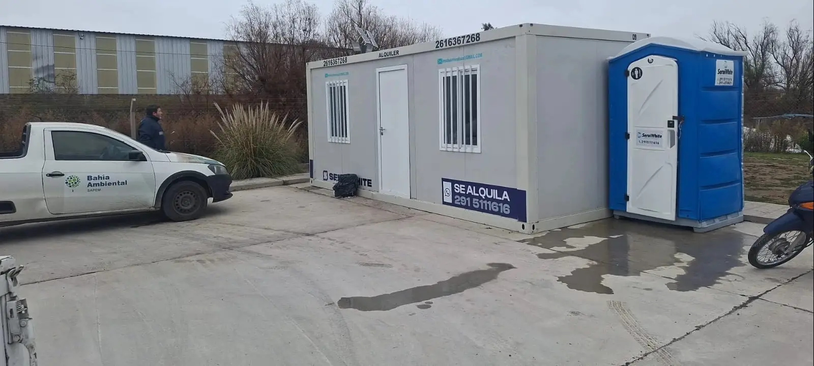 Módulo oficina Serviwhite con ventanas enrejadas y un baño químico al lado, en un predio industrial