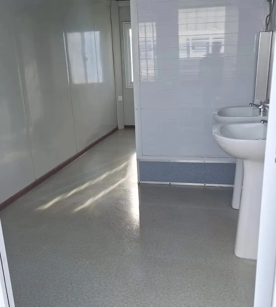 Interior de un módulo sanitario con dos lavatorios, tabique de boxes y piso vinílico