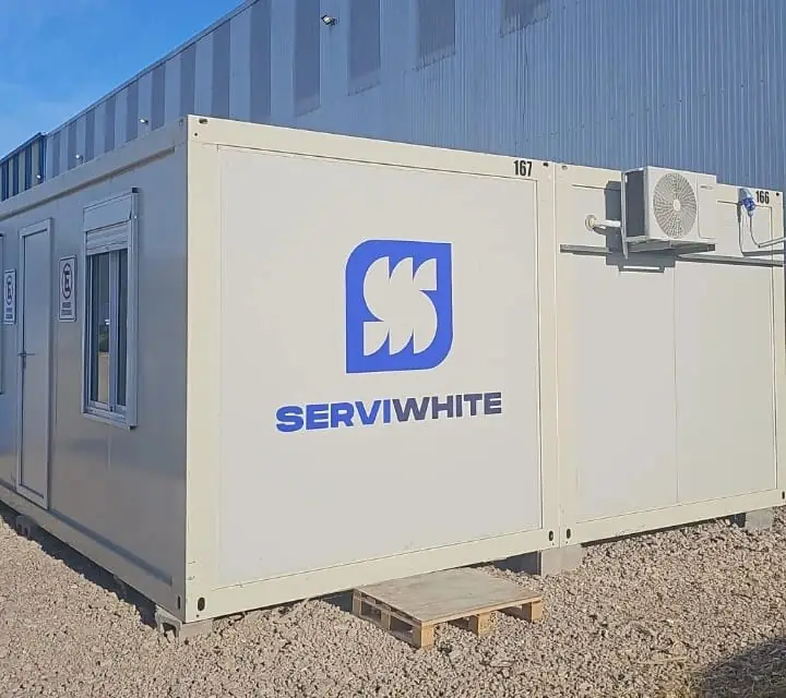 Dos módulos unidos con el logo de Serviwhite y aire acondicionado, junto a un galpón industrial