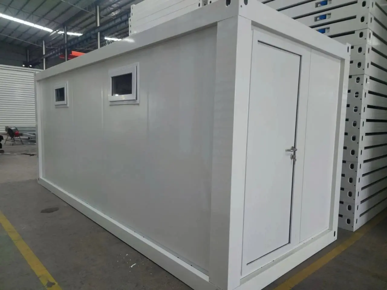 Módulo sanitario blanco con puerta y ventanas altas, terminado en fábrica