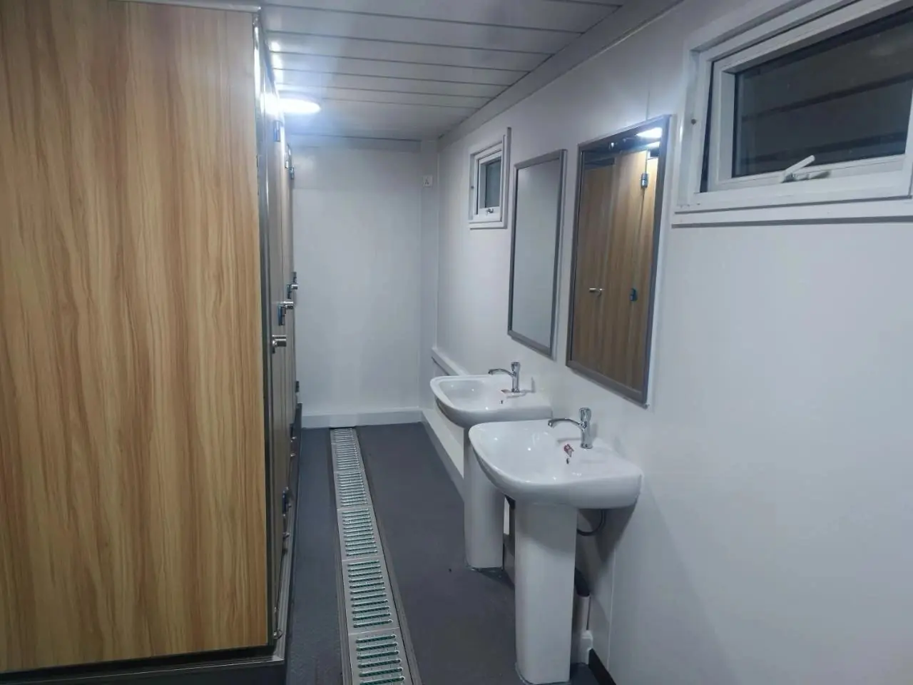 Dos lavatorios con espejo y boxes de inodoro en un módulo sanitario