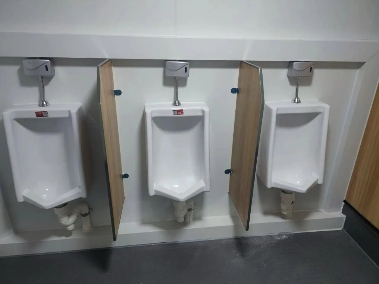 Tres mingitorios con descarga automática por sensor y divisores en un módulo sanitario