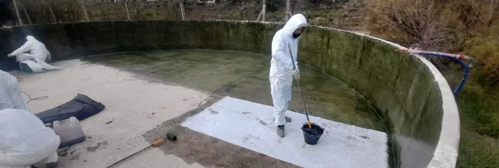 Operarios con mameluco descartable aplican revestimiento de PRFV en el fondo de una cisterna de hormigón