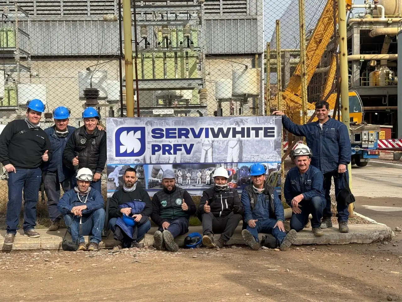 Diez operarios de Serviwhite PRFV posan con su banner frente a una planta industrial