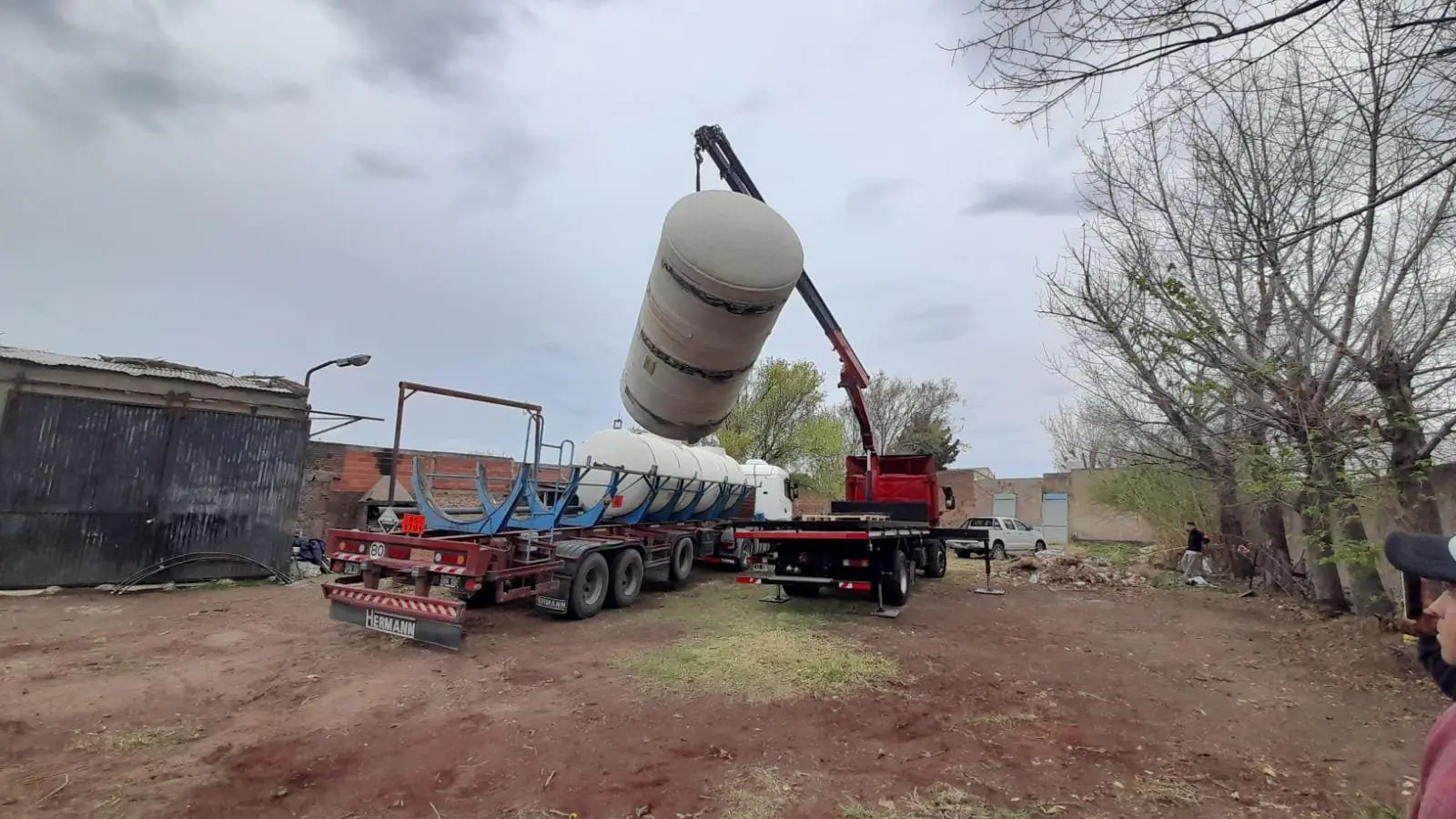 Hidrogrúa sobre camión izando un tanque cilíndrico de PRFV junto a un semirremolque con tanques