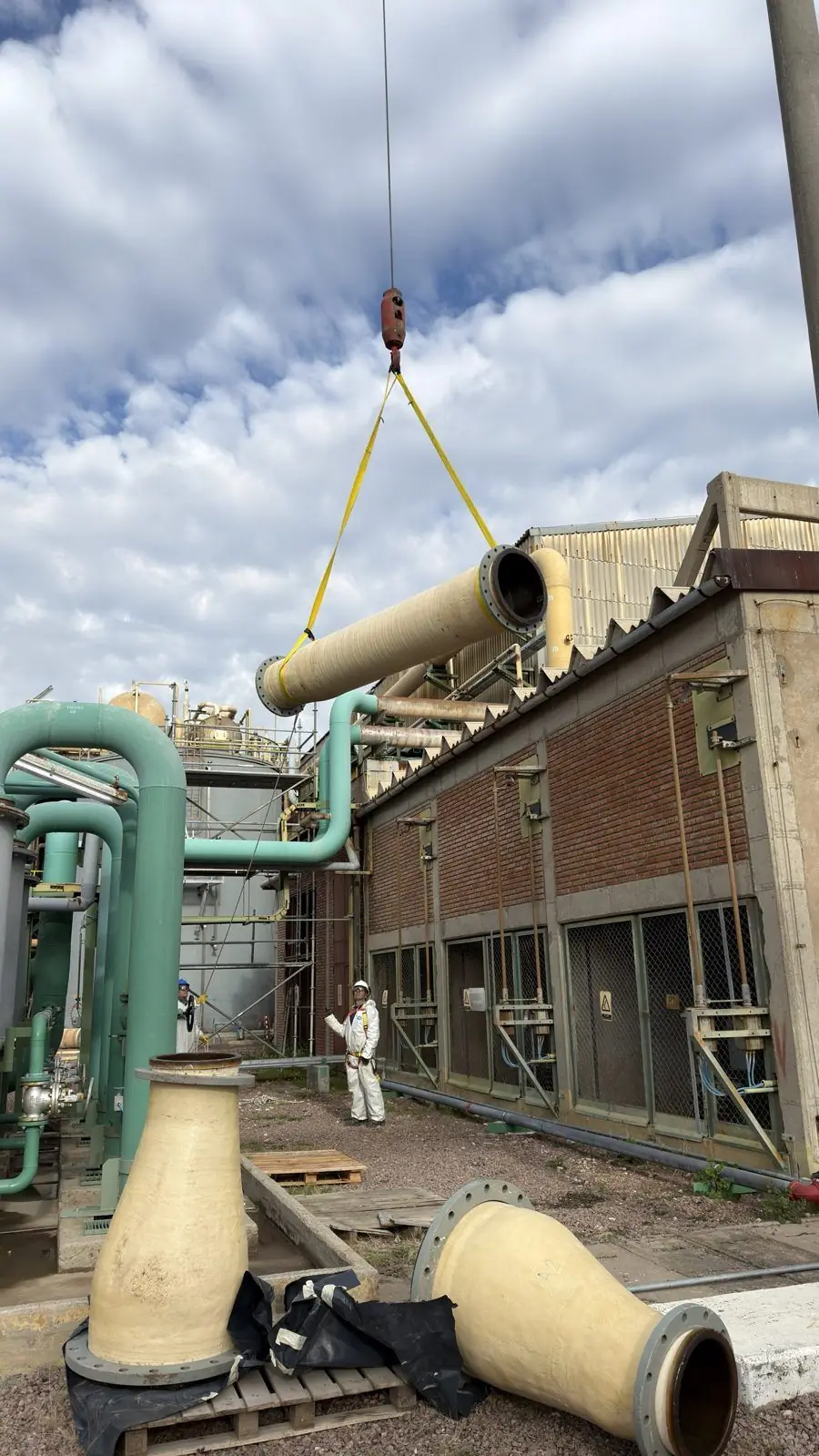Izaje de un caño de PRFV con eslingas en planta industrial; adelante, reducciones de PRFV