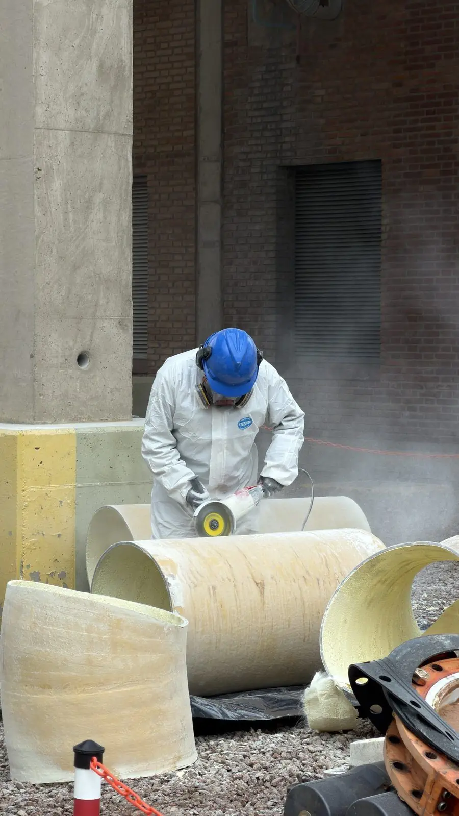 Operario con casco y máscara amolando un caño de PRFV entre otros tramos de cañería