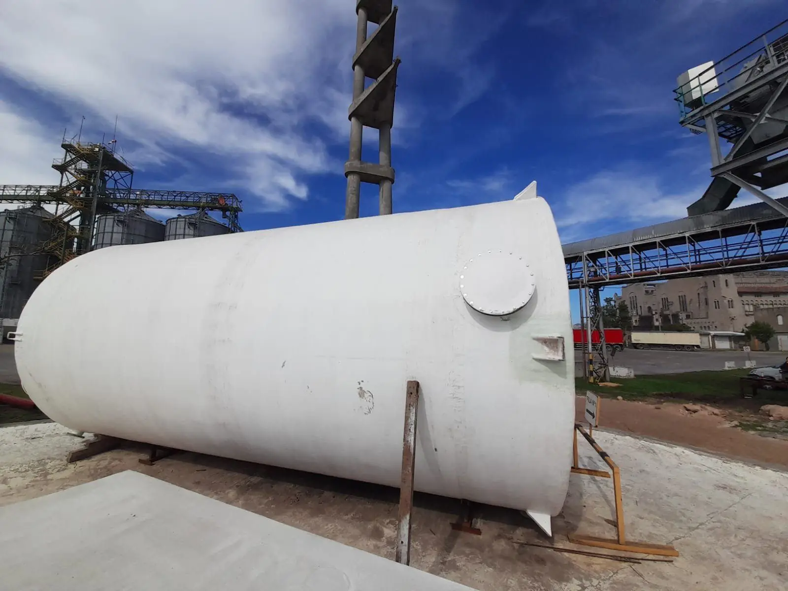 Tanque horizontal de PRFV blanco con boca de hombre, apoyado en una planta con silos